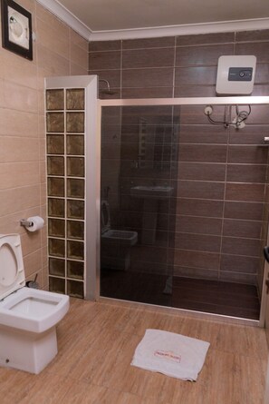 A bathroom with a toilet, a shower enclosure, and a towel on the floor. - Cotton Suites (Lagos)