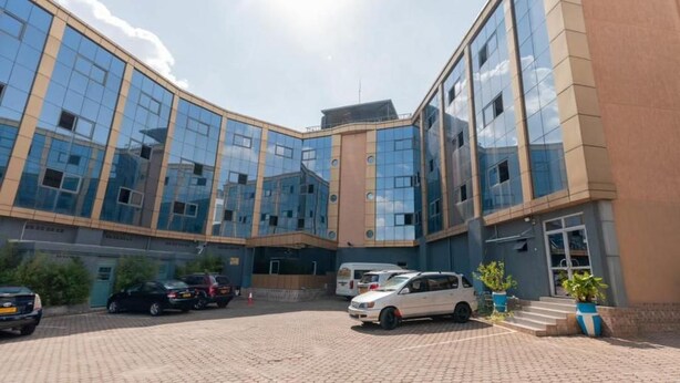 A modern building with a curved facade, a paved courtyard, and several parked cars. - Gihozo Hotel (Kigali)