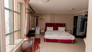 A hotel room with a bed, a desk, a chair, a wardrobe, and a window with curtains. - Gihozo Hotel (Kigali)