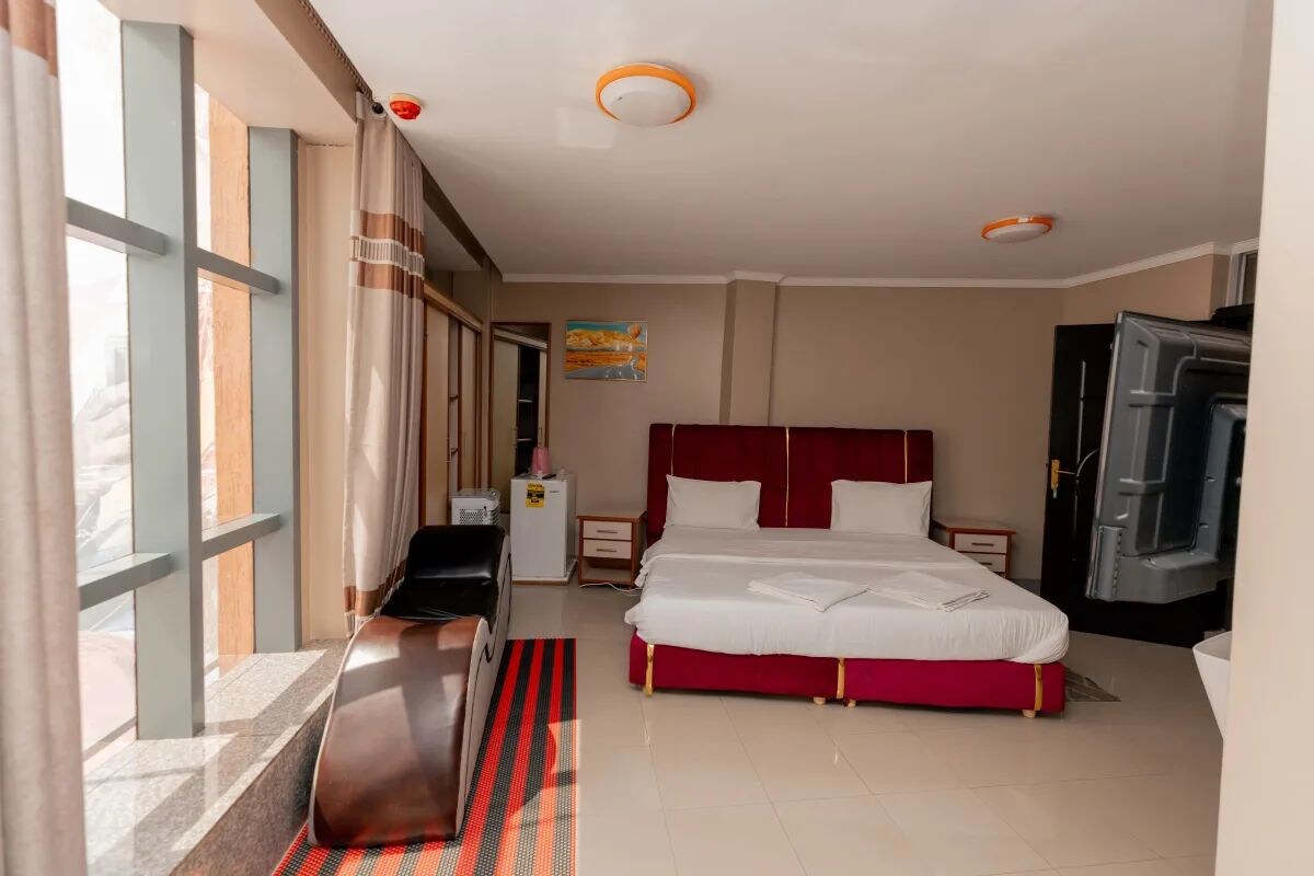 A hotel room with a bed, a desk, a chair, a wardrobe, and a window with curtains.