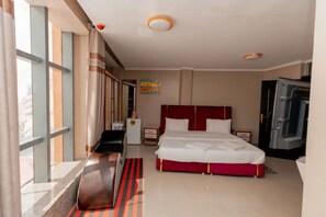 A hotel room with a bed, a desk, a chair, a wardrobe, and a window with curtains. - Gihozo Hotel (Kigali)