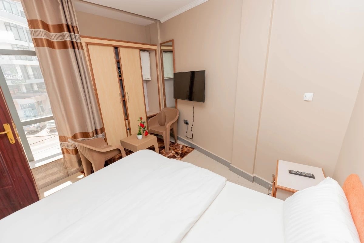 A hotel room with a bed, a desk, a chair, a TV, and a window with curtains.
