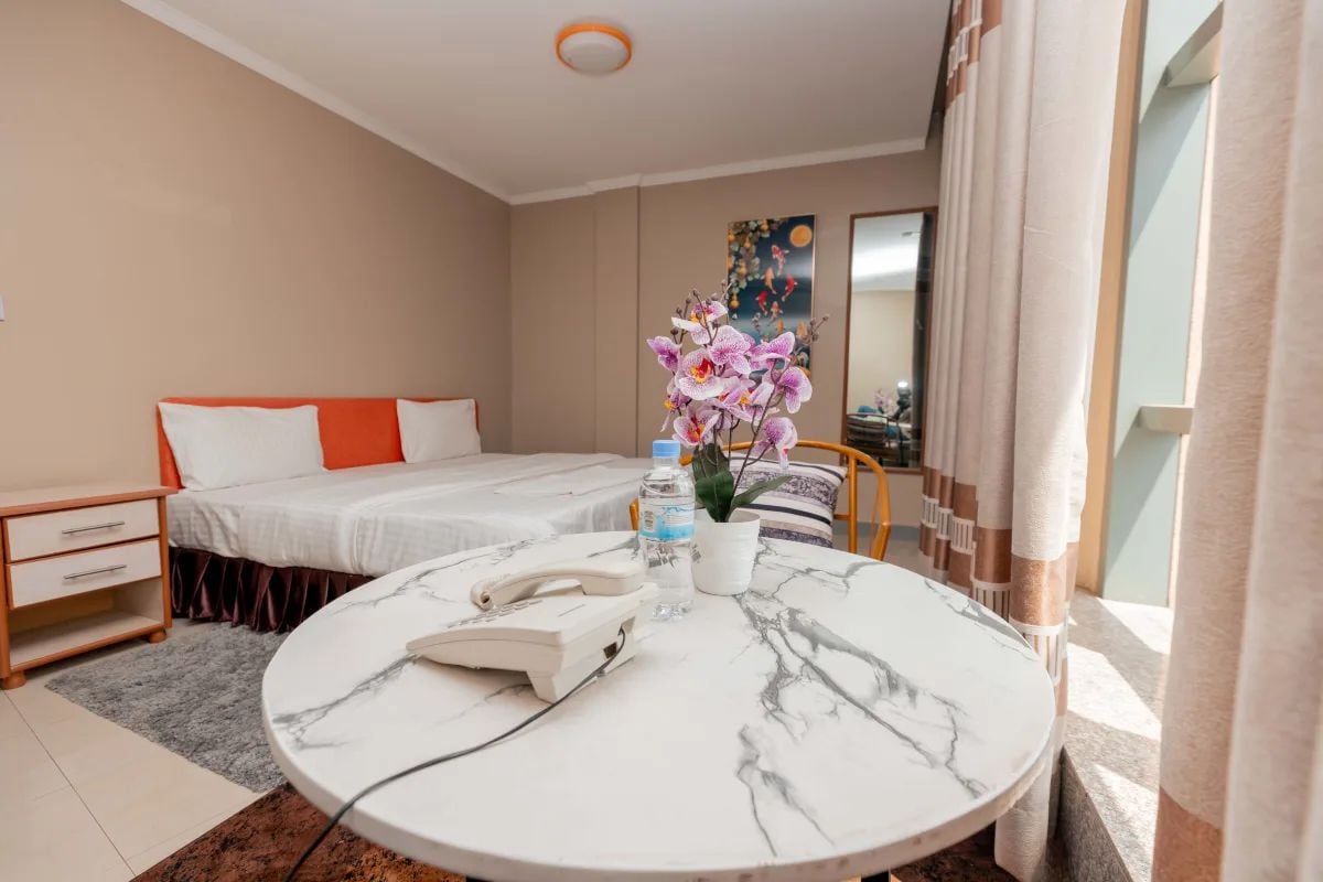 A hotel room with a bed, bedside table, and a round table with a phone and water bottle.