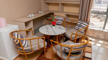 Quarto com uma mesa redonda, quatro cadeiras, um pequeno vaso com flores, uma chaleira e um telefone em uma prateleira.