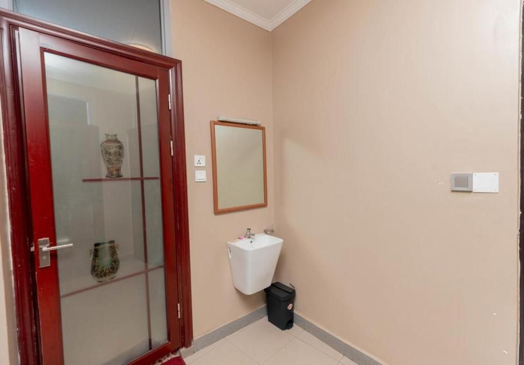 A bathroom with a glass door, a white sink, a mirror, and a trash bin.