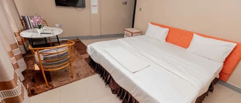 Habitación de hotel con una cama, un televisor montado en la pared, una mesita con una silla y una alfombra.