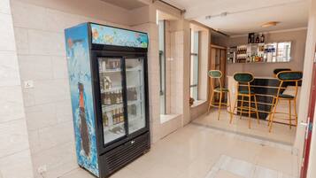 Um saguão de hotel com minibar, área de bar com banquetas e exposição de bebidas engarrafadas.