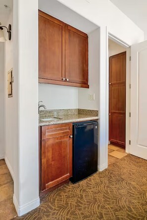 A compact kitchen with wooden cabinets, a granite countertop, and a black dishwasher. - Legacy Villas Studio En-suite with Fireplace,Patio, Pools, Kitchenette, Grnd Flr (La Quinta)