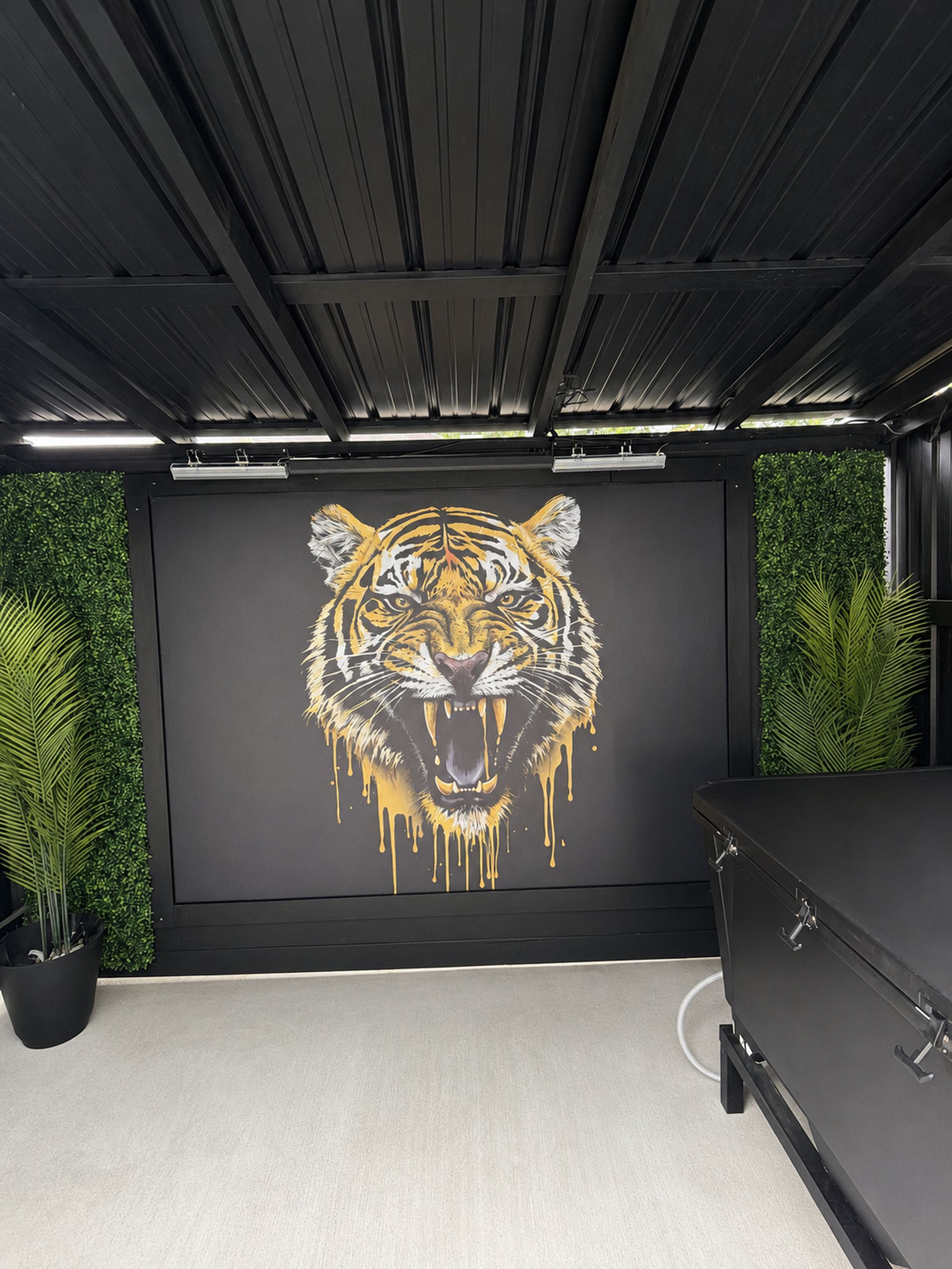 Quarto com um grande mural de tigre na parede, um armário preto e plantas verdes.