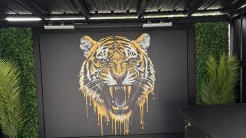Quarto com um grande mural de tigre na parede, um armário preto e plantas verdes.