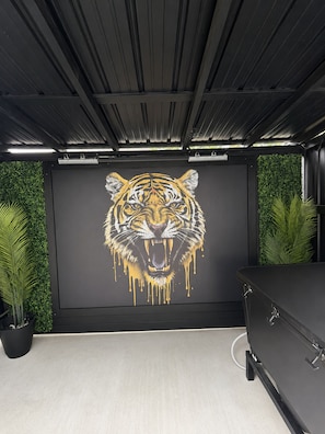 Quarto com um grande mural de tigre na parede, um armário preto e plantas verdes.