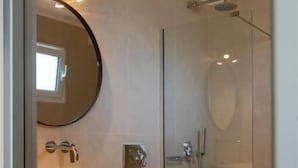 A modern bathroom with a glass shower enclosure, a round mirror, and a white sink. - Elina Hotel Perdika (Igoumenitsa)