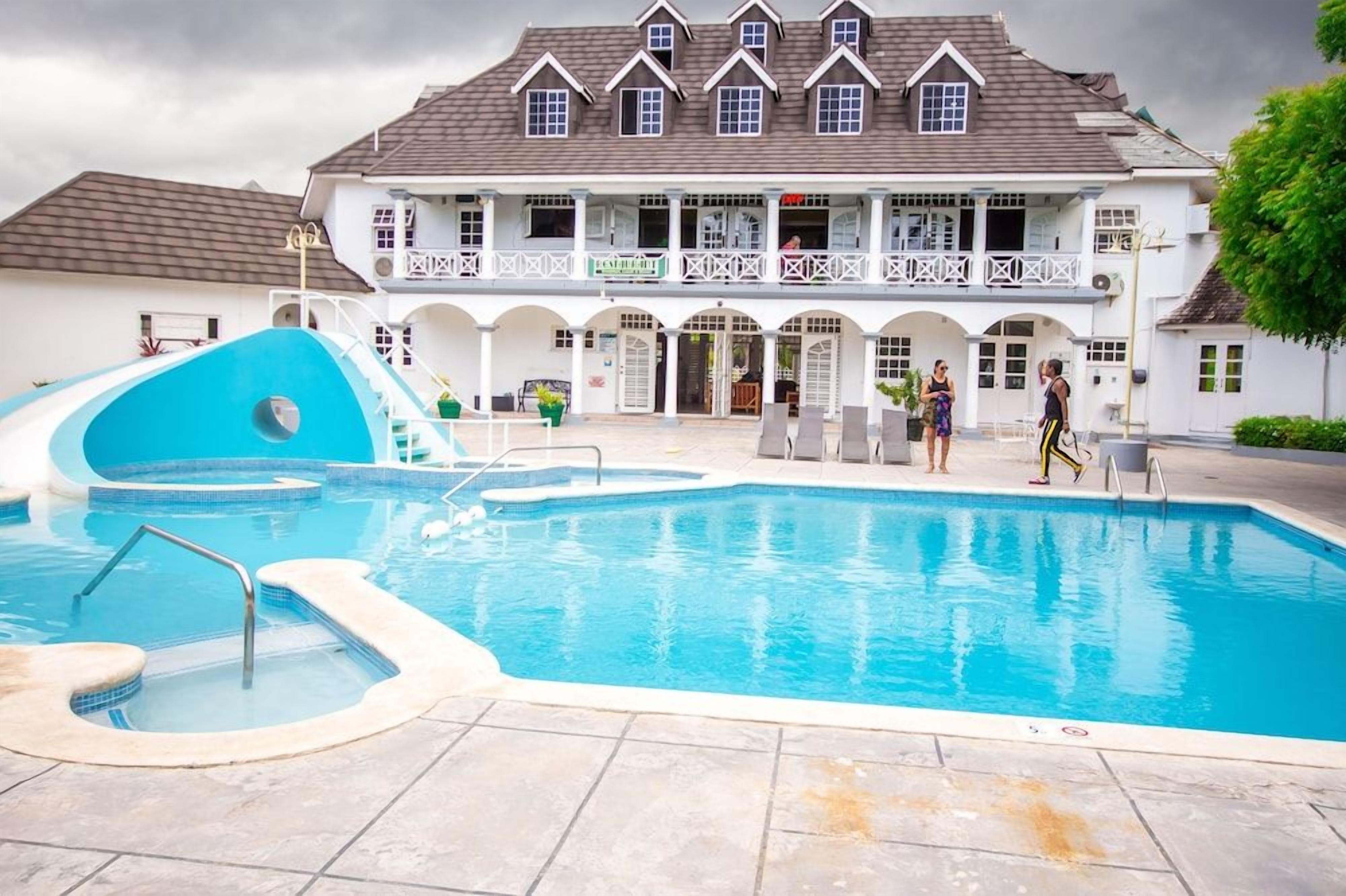 Uma piscina com escorrega, um edifício com várias varandas e algumas pessoas.