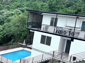 A two-story building with a swimming pool, surrounded by dense greenery. - Mountain Oasis-Farm Stay solar powered with swimming pool. Quiet and peaceful. (San German)