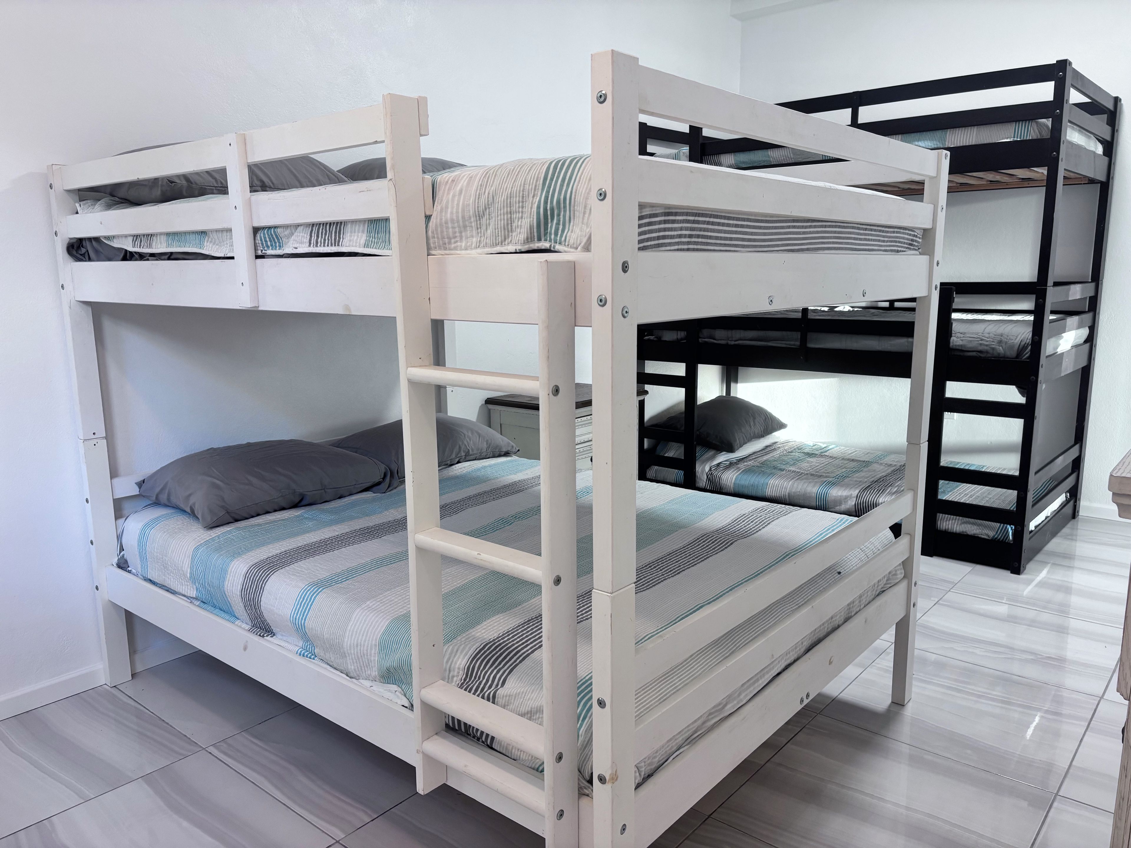 A bunk bed with a white frame and striped bedding, a white wardrobe, and a tiled floor.