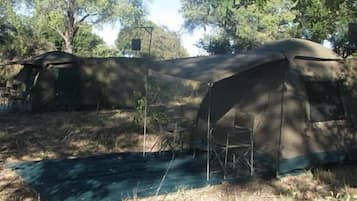 A tented camping area with a table and chairs, surrounded by trees.