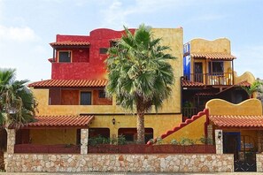 A multi-story building with a stone base, red and yellow walls, and a palm tree in front. - Sakaroule Bed and Breakfast (Sal)
