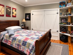 Une chambre à coucher avec un lit en bois, une table de chevet, une lampe, une armoire et une étagère où sont exposés des trophées et des objets de collection.