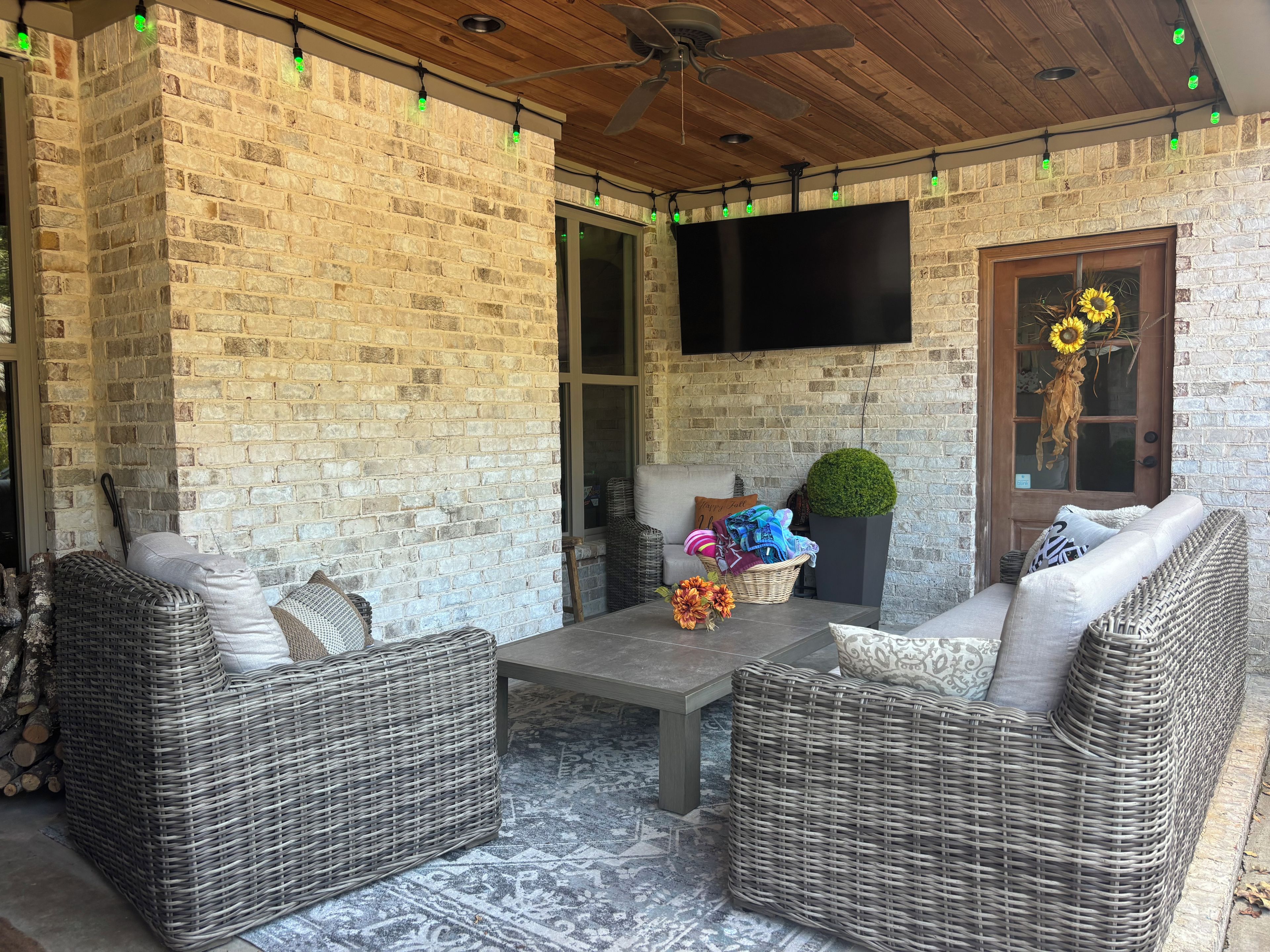 Une terrasse couverte avec des meubles en osier, un téléviseur à écran plat et un mur en briques.