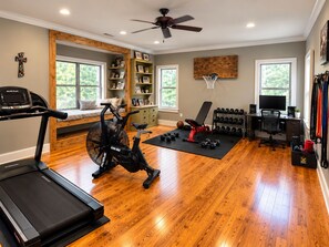 Une salle de sport à domicile équipée de matériel d’exercice, d’un tapis de course, d’un vélo d’appartement, d’un banc de musculation et d’un support à poids.