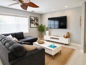 A modern living room with a grey sofa, a white coffee table, a flat-screen TV, and a ceiling fan. - Casa Palma - A South Florida Oasis (Deerfield Beach)