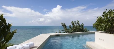 Céu azul límpido, piscina com vista para o mar e placa indicando profundidade de 1,2 metros.