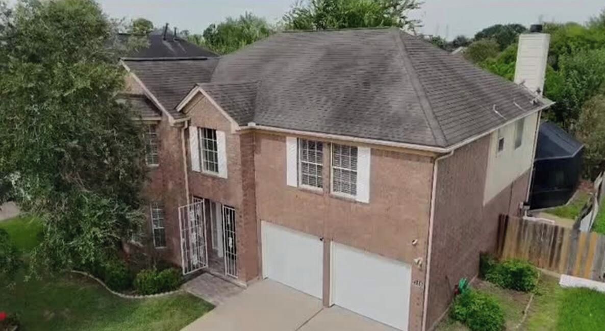 A two-story house with a garage, a fenced yard, and a large tree.