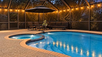 A swimming pool with a hot tub, surrounded by a covered patio with seating and string lights.