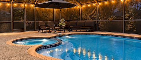 A swimming pool with a hot tub, surrounded by a covered patio with seating and string lights.