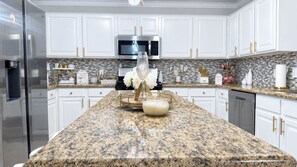 A modern kitchen with white cabinets, granite countertops, stainless steel appliances, and decorative items.