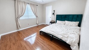 Quarto com cama, mesa de cabeceira, abajur e janela com cortinas.