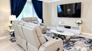A living room with a large flat-screen TV, a beige sofa, a coffee table, and a patterned rug.