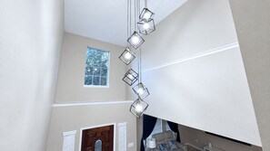 Interior moderno com luminária geométrica, janela com vista para árvores e porta com painel de vidro.