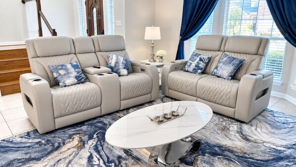 Een woonkamer met twee beige leren banken, een ronde salontafel en een vloerkleed met een blauw marmerpatroon.