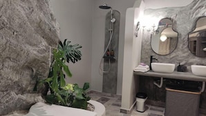 A bathroom with a stone wall, a shower, a sink, and a mirror. - Aegean Castle Suites Greek Hospitality Experience (Andros)