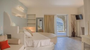 A hotel room with a curved bed, a sofa, a TV, a large window with a view, and a balcony. - Aegean Castle Suites Greek Hospitality Experience (Andros)