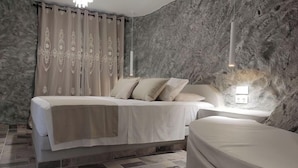 A bedroom with a bed, a bedside table, a lamp, and a stone-textured wall. - Aegean Castle Suites Greek Hospitality Experience (Andros)