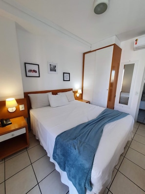 A hotel room with a bed, bedside table, lamp, and wall-mounted artwork. - Bristol Praia do Canto (Vitoria)