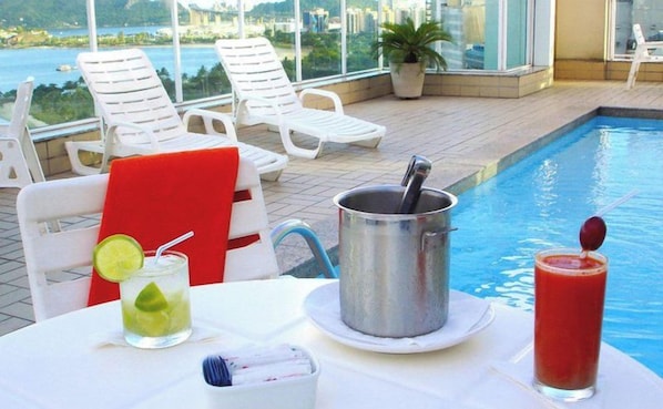 A poolside table with a drink, a metal container, and a red towel. - Bristol Praia do Canto (Vitoria)