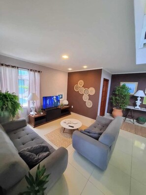 A modern living room with a flat-screen TV, two sofas, a coffee table, and decorative wall art. - Pousada Algarve (Cabo Frio)