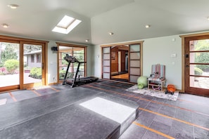 Um quarto amplo com esteira ergométrica, bolas de exercício e tapete de yoga.