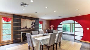 A dining area with a table set for six, a fireplace, and a large window with a view of greenery. - Stunning Lake View 3BR Home with Serene Japanese Garden & Pond (Lake View)