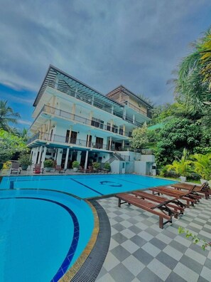 Um hotel com piscina, espreguiçadeiras e um edifício de vários andares com varandas.