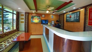 Un'area reception di un hotel con un bancone, posti a sedere e un televisore.