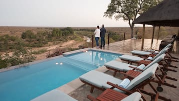 A pool with lounge chairs and a couple standing by the poolside.