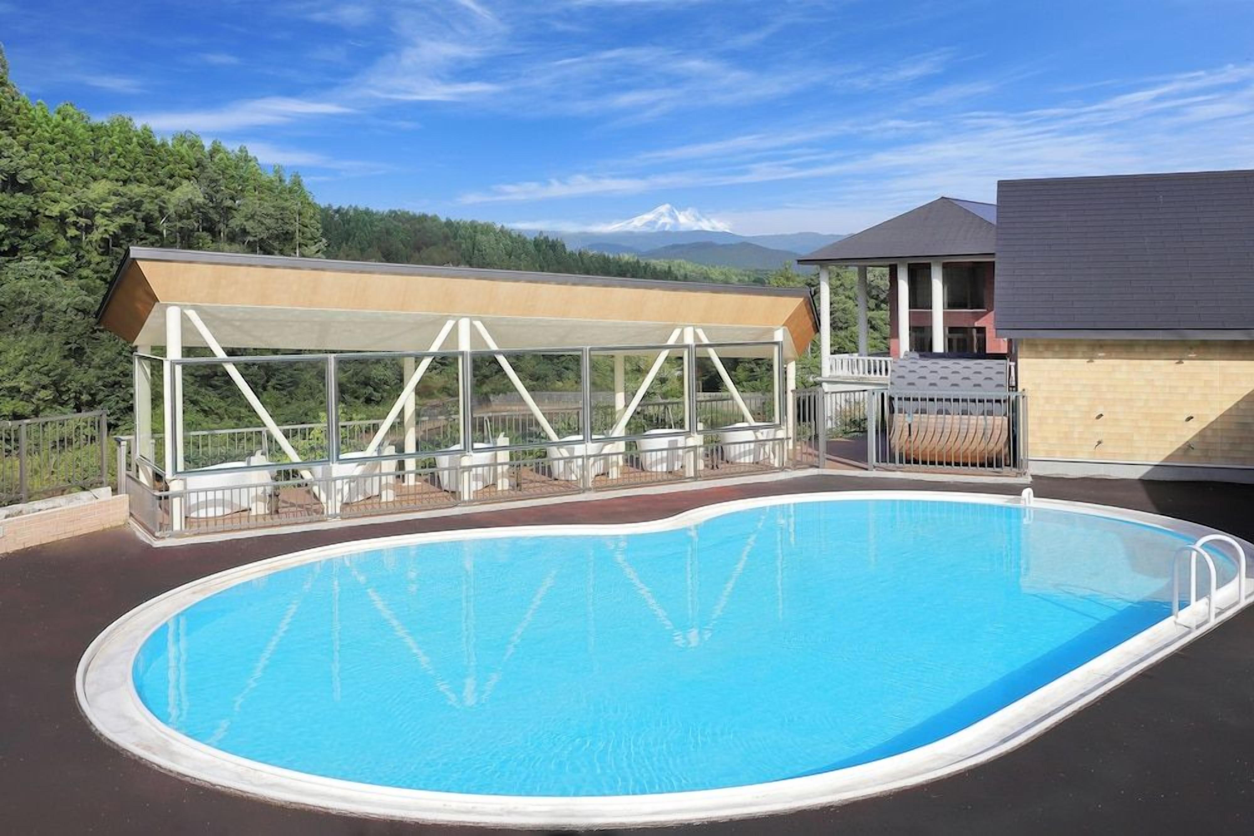 A swimming pool with a covered area, a building with a sloped roof, and a mountainous backdrop.
