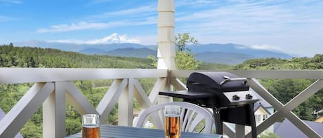 A balcony with a table, two glasses of a beverage, and a grill.