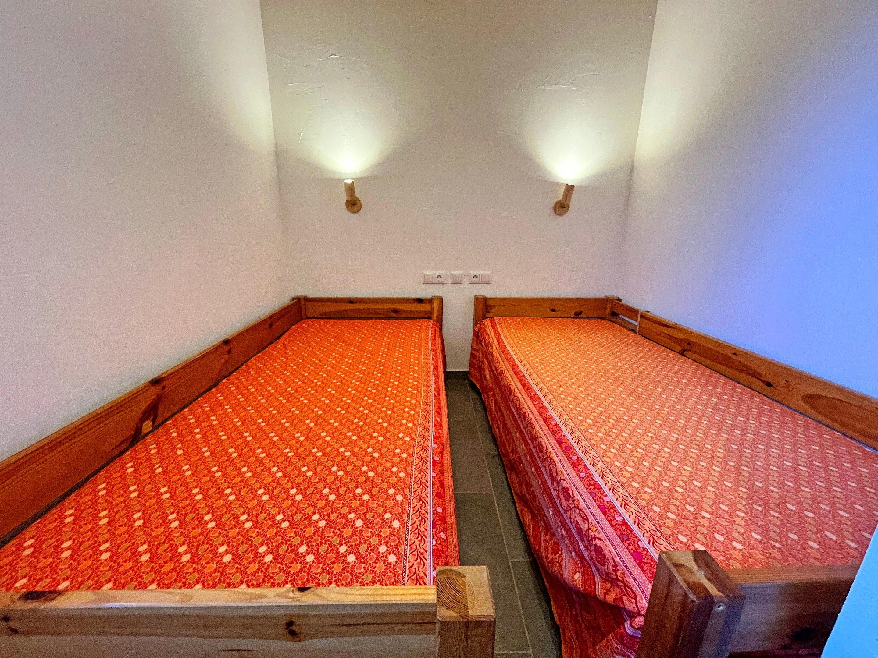 Une chambre double avec deux lits simples, chacun doté d’un cadre en bois et d’une couvre-lit à motifs.