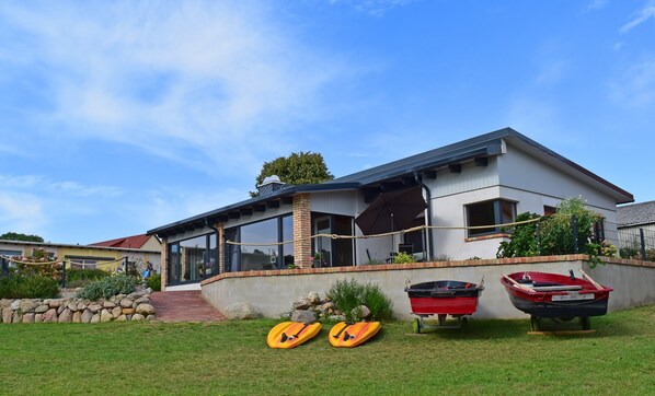 A modern two-story house with a covered porch, a stone retaining wall, and a grassy yard. - Holiday Apartment With Private Lake Access and Jetty (Warin)