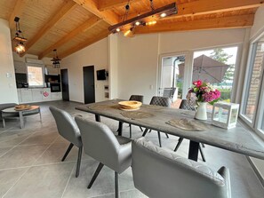 A spacious dining area with a long table, multiple chairs, and a modern kitchen in the background. - Holiday Apartment With Private Lake Access and Jetty (Warin)